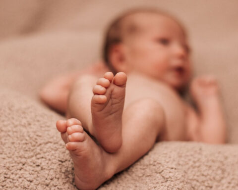 Close-up of a newborn baby's feet while lying on a soft beige blanket.