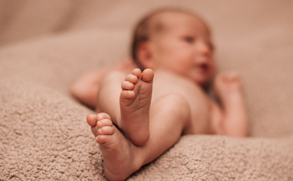 Close-up of a newborn baby's feet while lying on a soft beige blanket.