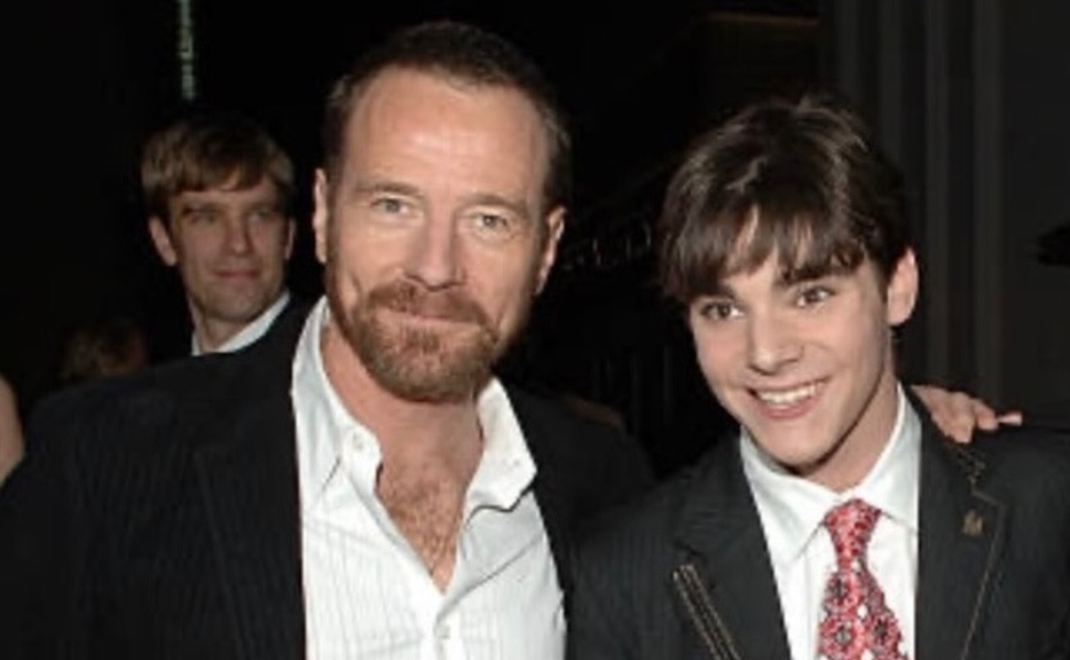 Bryan Cranston and RJ Mitte smiling together at an event, both wearing suits.