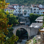 Historic stone bridge in Mostar, Bosnia and Herzegovina, surrounded by colorful autumn trees and traditional buildings.