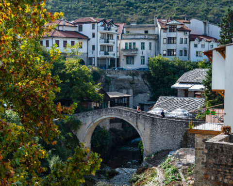 Historic stone bridge in Mostar, Bosnia and Herzegovina, surrounded by colorful autumn trees and traditional buildings.