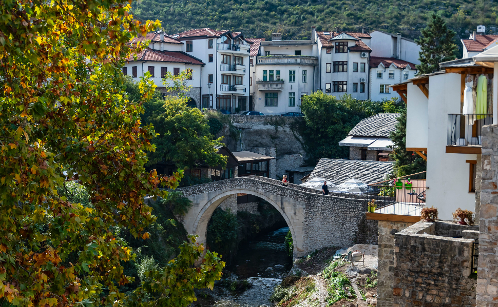 Historic stone bridge in Mostar, Bosnia and Herzegovina, surrounded by colorful autumn trees and traditional buildings.