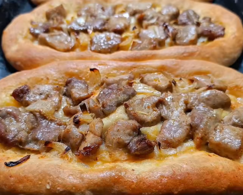 Two freshly baked Macedonian pastrmajlija flatbreads topped with roasted pork pieces and onions on a baking tray.