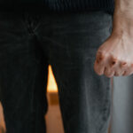 Close-up of a person with a clenched fist and visible injuries on their knuckles, illustrating physical violence.
