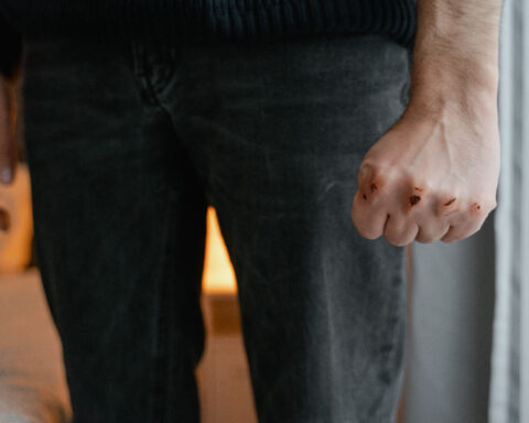 Close-up of a person with a clenched fist and visible injuries on their knuckles, illustrating physical violence.