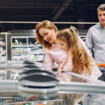 Family shopping for groceries at a supermarket and looking at products in a freezer.