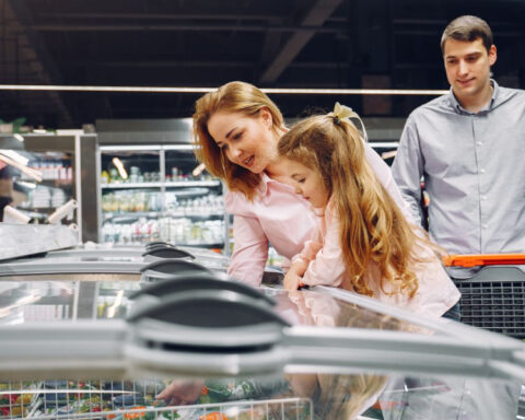 Family shopping for groceries at a supermarket and looking at products in a freezer.
