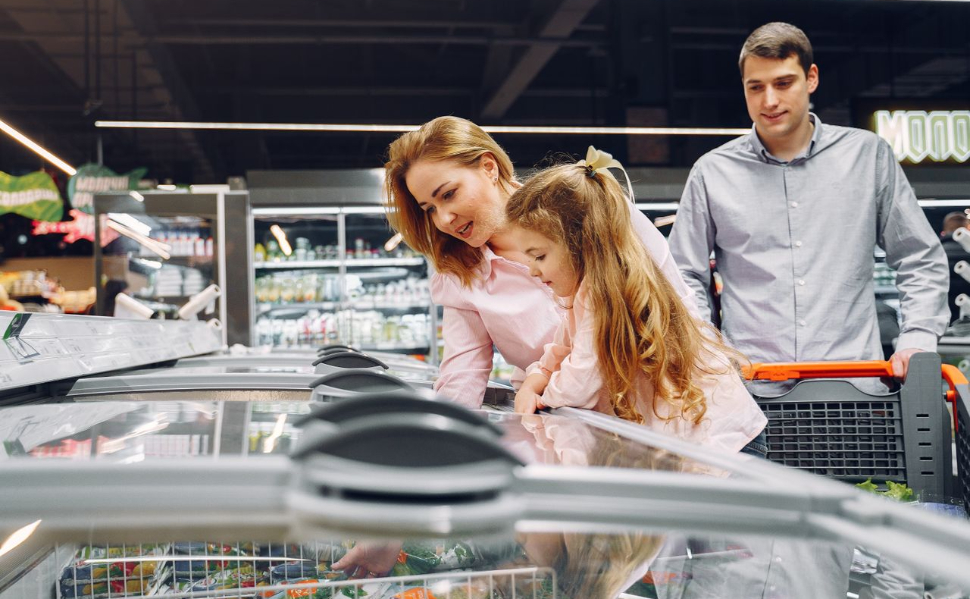 Family shopping for groceries at a supermarket and looking at products in a freezer.