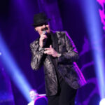 Bosnian singer Haris Dzinovic performing on stage with a microphone, wearing his signature black hat.