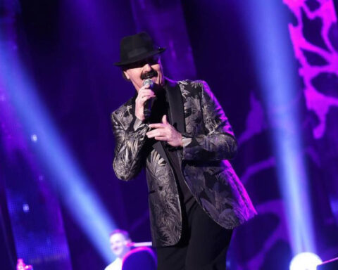 Bosnian singer Haris Dzinovic performing on stage with a microphone, wearing his signature black hat.