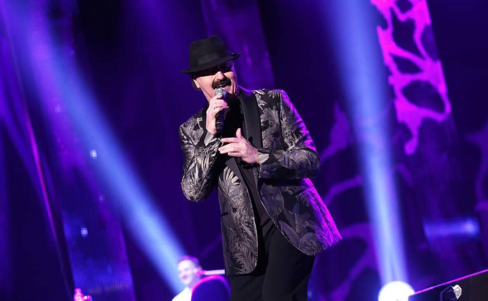 Bosnian singer Haris Dzinovic performing on stage with a microphone, wearing his signature black hat.