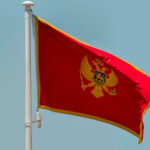 National flag of Montenegro waving on a flagpole against a clear blue sky.