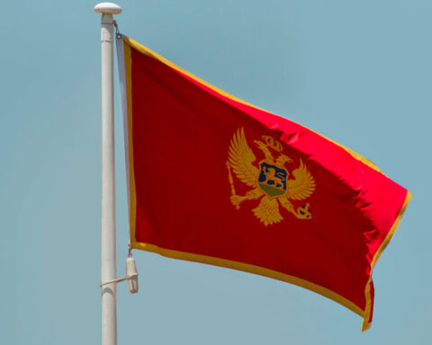 National flag of Montenegro waving on a flagpole against a clear blue sky.