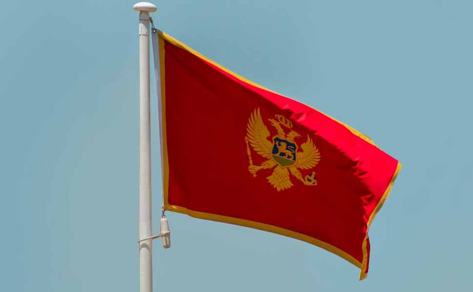 National flag of Montenegro waving on a flagpole against a clear blue sky.