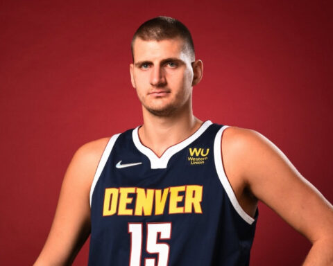 Serbian NBA star Nikola Jokić wearing his Denver Nuggets No. 15 jersey and holding a basketball against a red background.