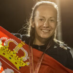 Serbian women's minifootball player smiling while holding the Serbian national flag and wearing a medal.