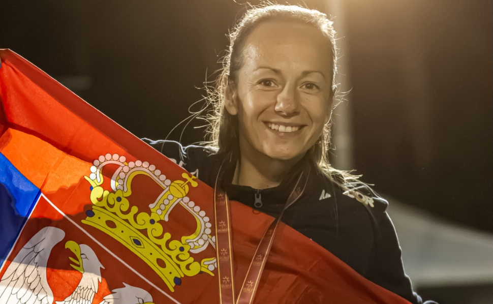 Serbian women's minifootball player smiling while holding the Serbian national flag and wearing a medal.