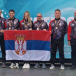 Serbian paragliders posing with the Serbian national flag and their medals at the 2026 European Paragliding Accuracy Championship in Romania.