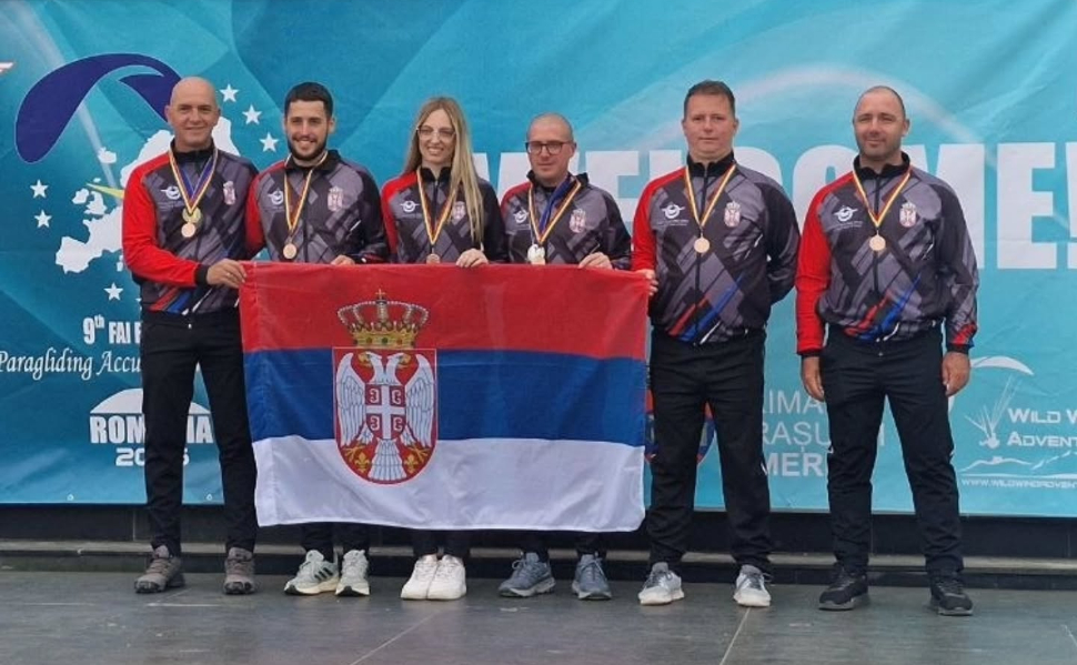 Serbian paragliders posing with the Serbian national flag and their medals at the 2026 European Paragliding Accuracy Championship in Romania.