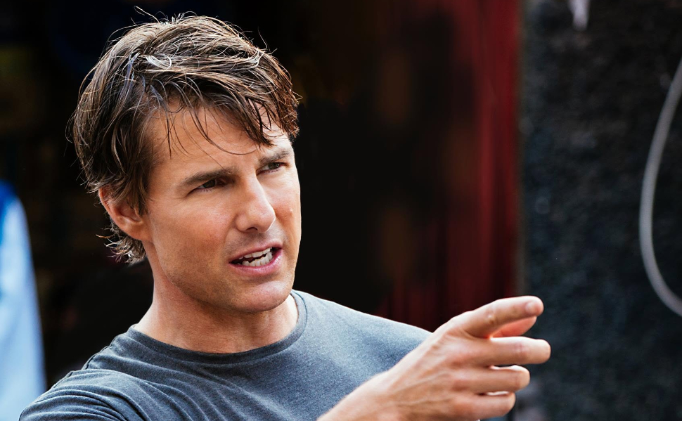 Hollywood actor Tom Cruise wearing a gray T-shirt and pointing during a conversation.