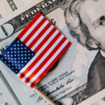 Small American flag resting on US dollar banknotes, including a twenty-dollar bill.
