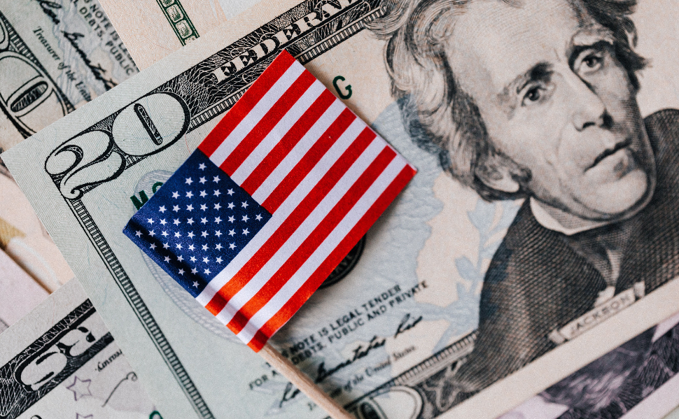 Small American flag resting on US dollar banknotes, including a twenty-dollar bill.
